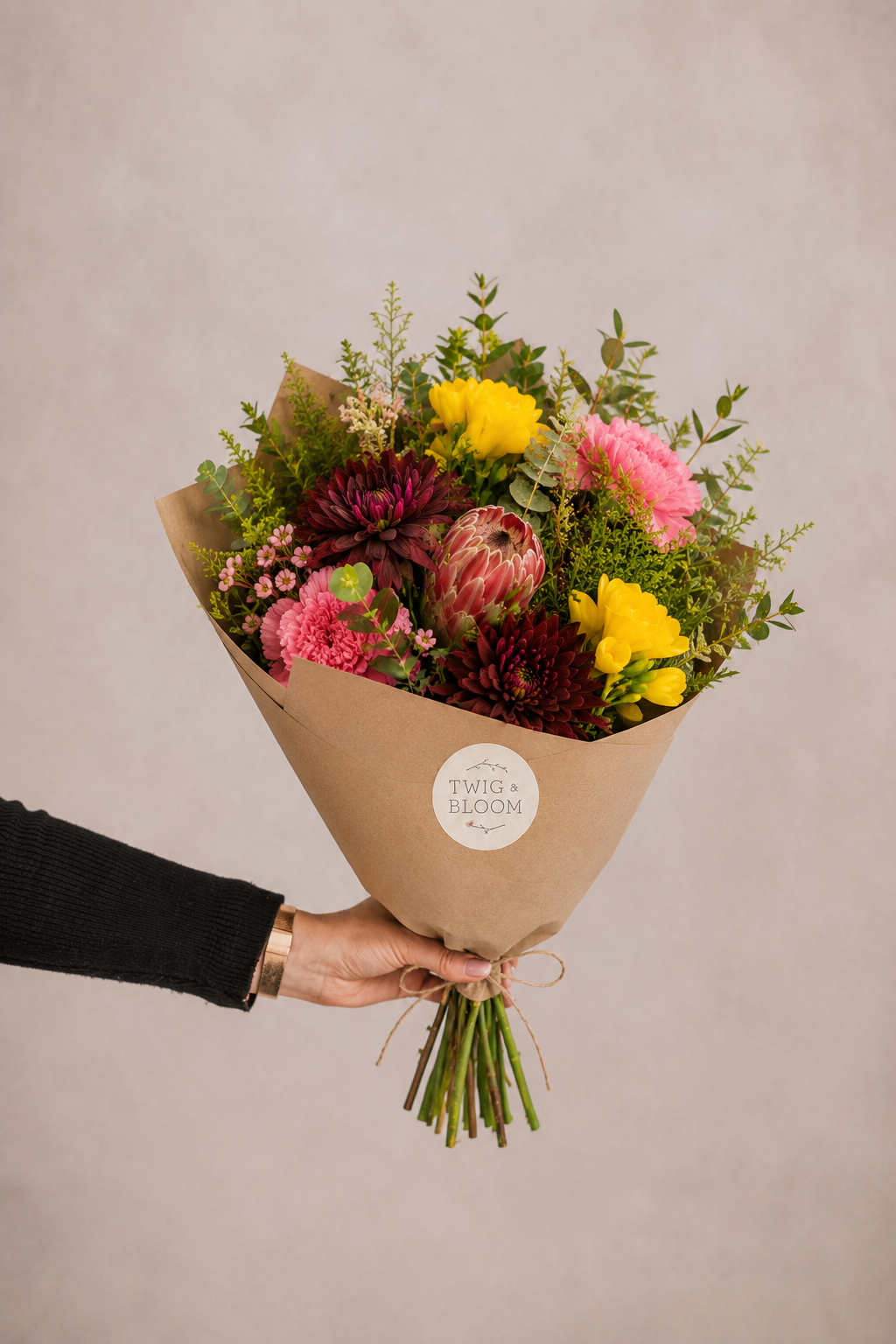 Bouquet of flowers wrapped in brown paper held by a person against a plain background