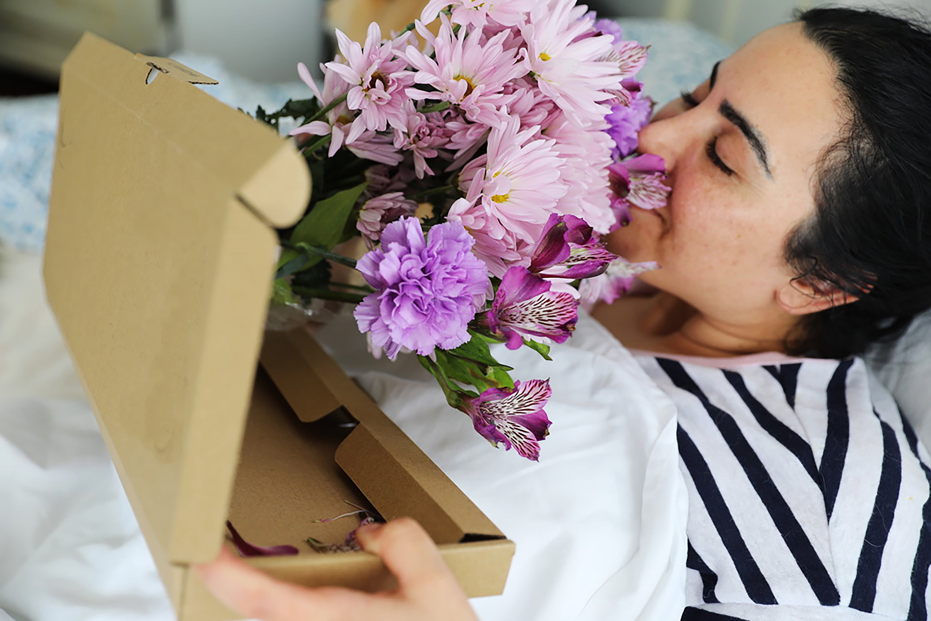 Sick woman in bed smelling fresh flowers
