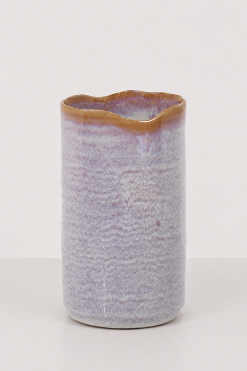A handmade ceramic vase with a wavy, irregular rim, featuring a textured lavender-purple body with a glossy brown glazed top, set against a plain light gray background.