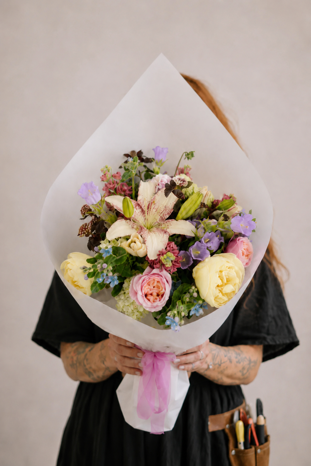 Person holding a bouquet of flowers wrapped in white paper against a plain background