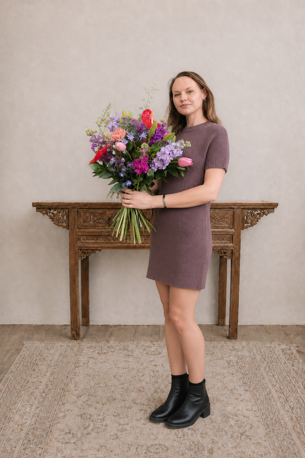 Woman holding a bouquet of flowers in a room with a wooden table and beige wall.