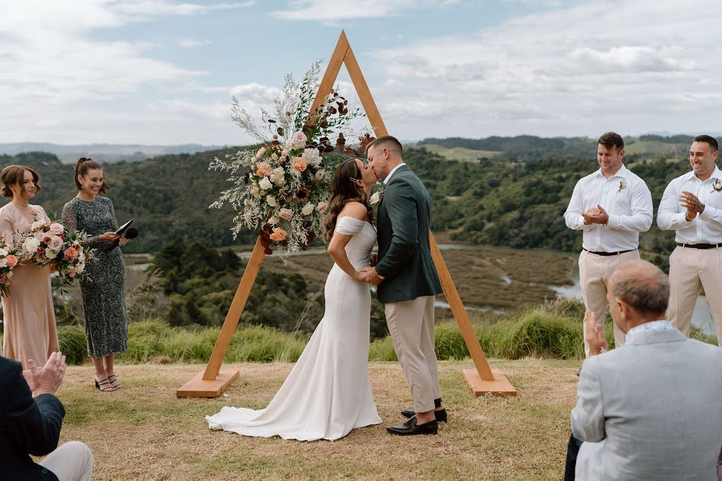 Newly married couple kissing in front of wedding arch with fresh flowers