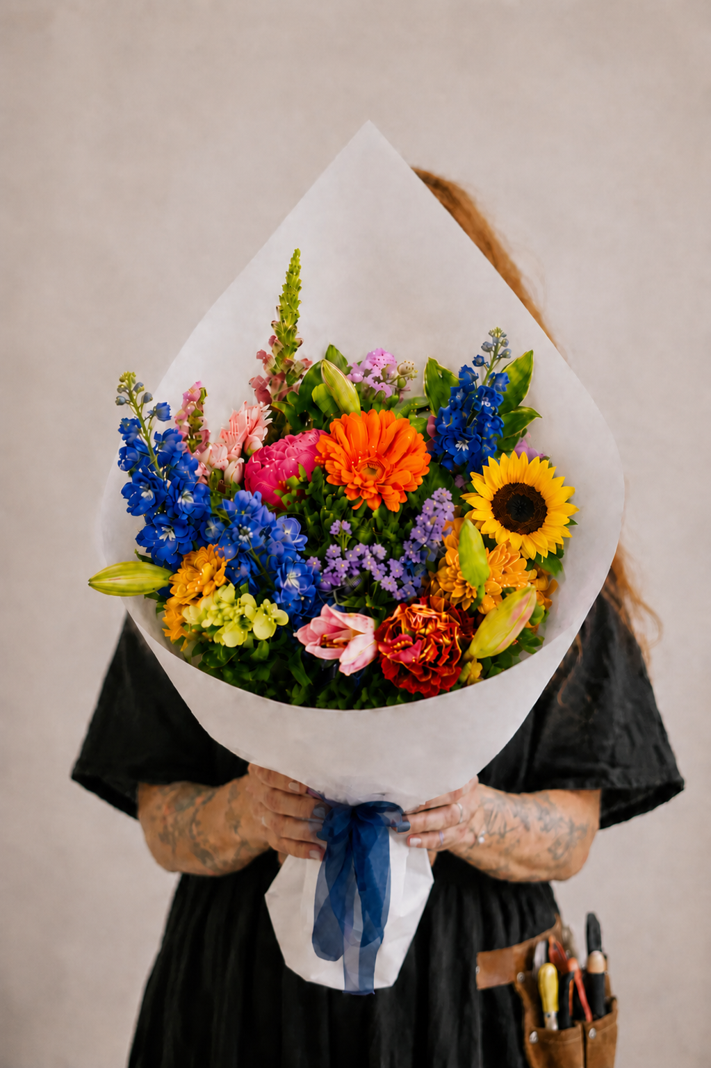 Person holding a colorful bouquet of flowers wrapped in white paper against a neutral background
