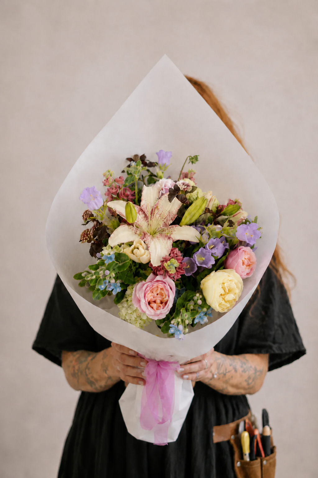 Person holding a bouquet of flowers wrapped in white paper against a plain background