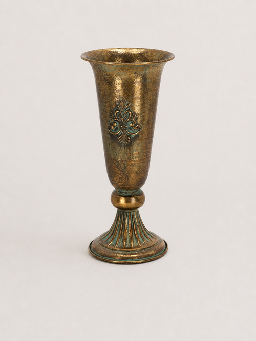 An antique-style bronze goblet or cup with a flared rim, decorative relief motif on the body, and a ribbed pedestal base, shown against a plain light background.