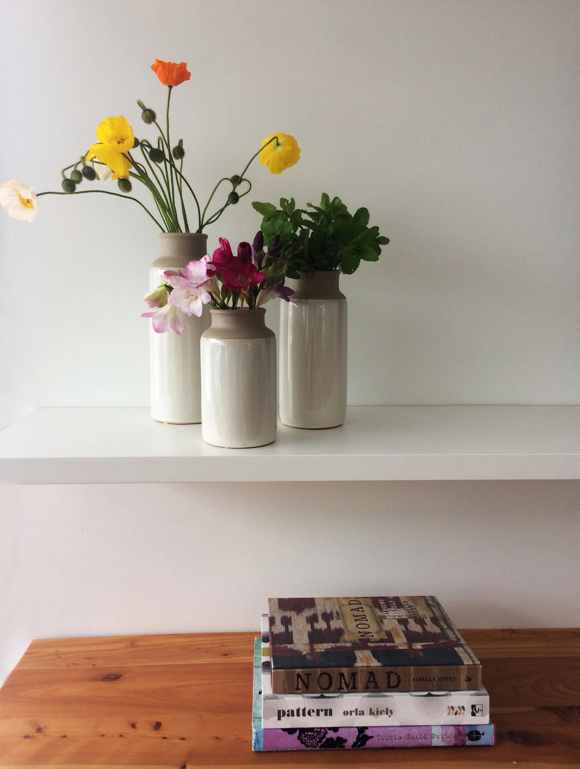 Three ceramic potter vase bottles on a shelf with fresh flowers in them