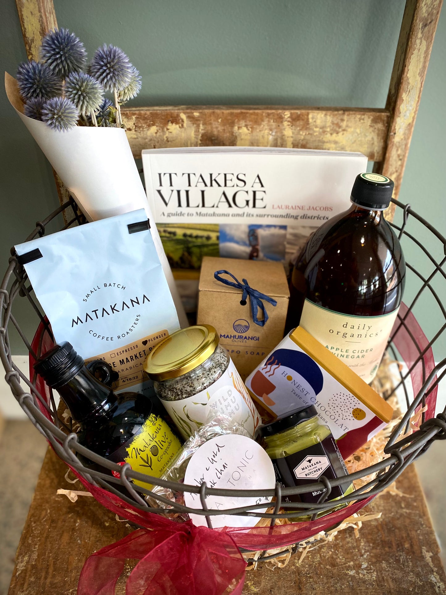 Wire hamper with Matakana olive oil, Matakana Coffee Roasters coffee, Daily Organics apple cider, Tea & Tonic Chai tea, Mahurangi Allepo soap, Matakana Butchers' mustard, Honest Chocolates, dried flowers, Wild Rimu Rimu salt and It Takes A Village book.