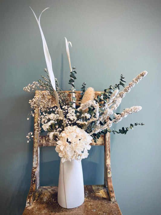 Green and white dried flower arrangement in a white ceramic vase